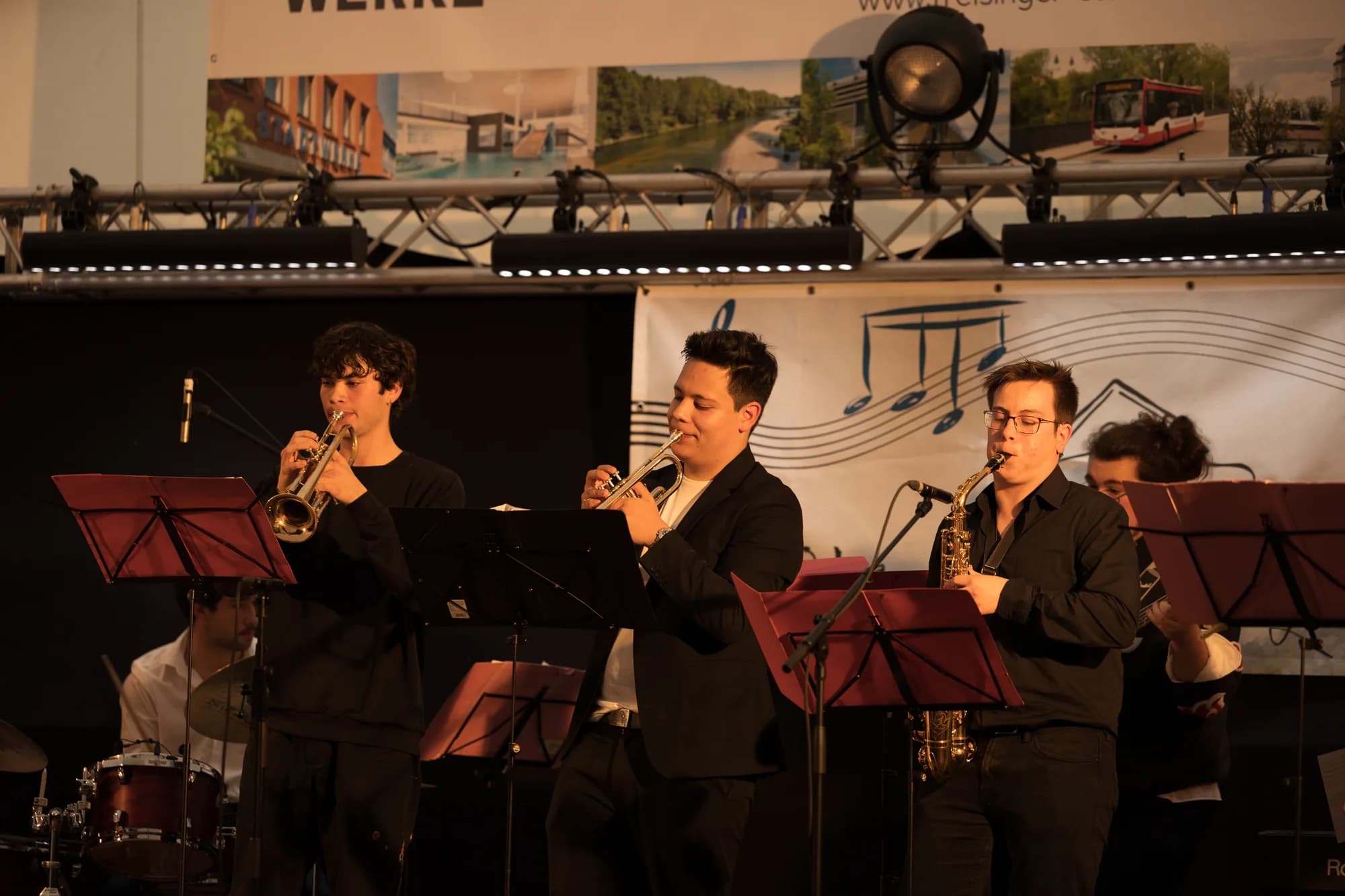 A brass band performs on stage with trumpeters and a saxophonist playing under warm lighting.
