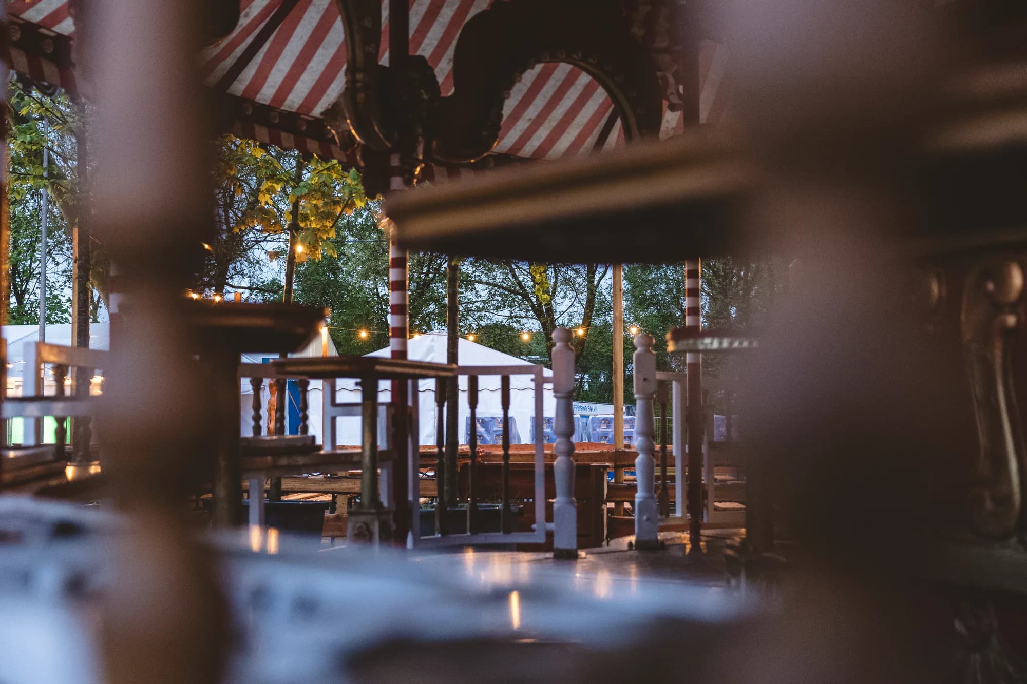 A view through the wooden railing of a carousel looking out onto the festival grounds at dusk.