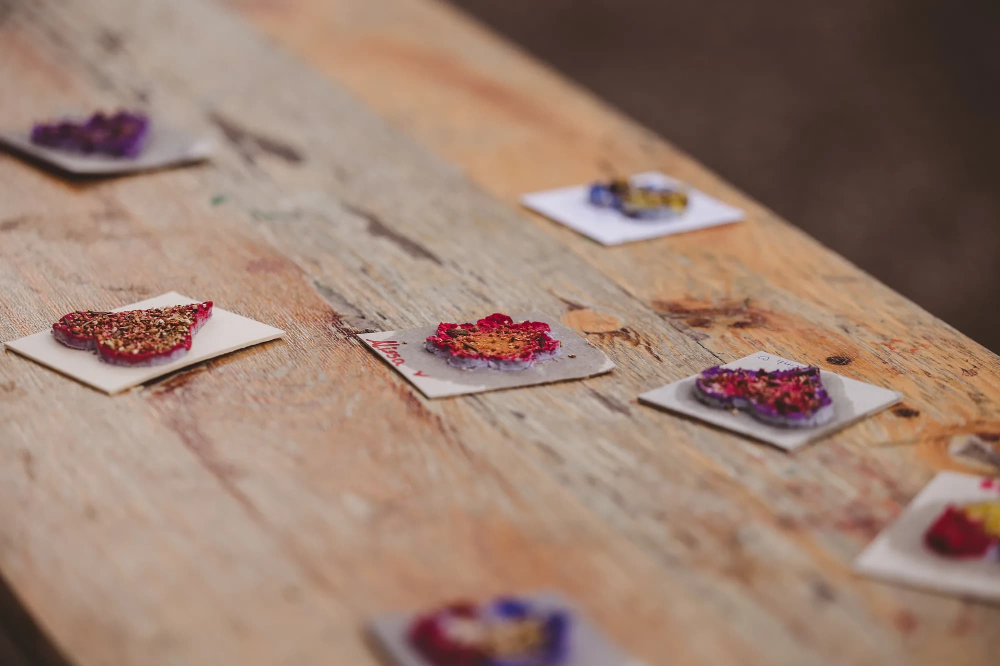 Colorful edible flower crafts arranged on small white squares on a rustic wooden table.