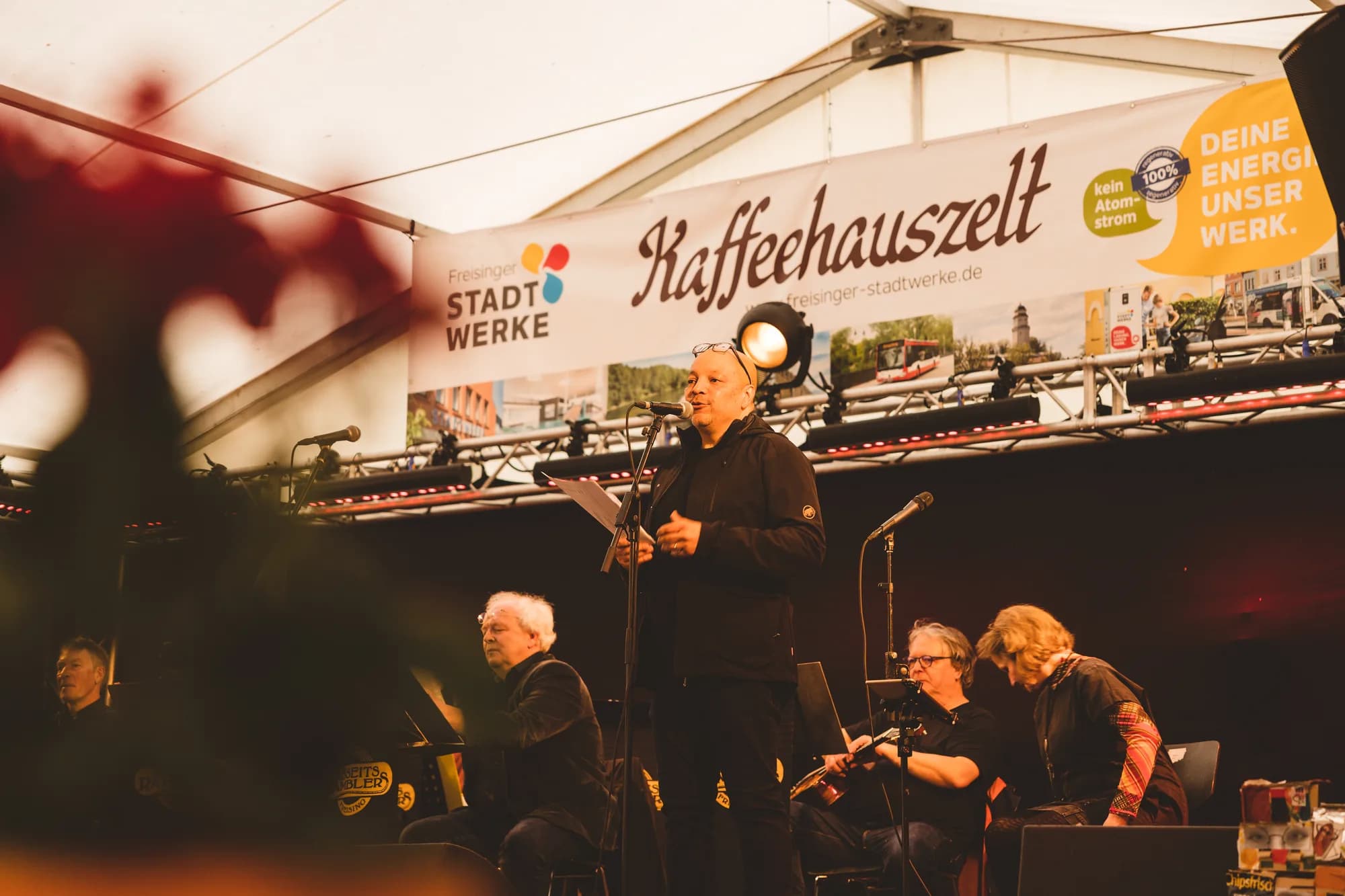 A folk band performs on stage inside the Kaffeehauszelt while a large crowd watches.